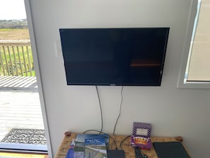 A flat-screen TV mounted on a wall with a view of a deck and outdoor area. - Short Walk to Tokerau (Karikari Peninsula)