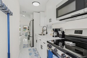 Cozinha moderna com armários brancos, geladeira de aço inoxidável, micro-ondas, cafeteira e fogão.