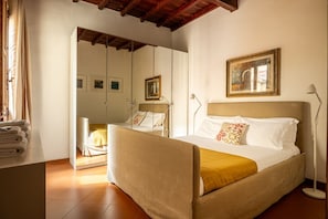 A bedroom with a bed, a bedside lamp, a mirror, and a window with curtains. - Casa Brunelleschi by Maison Florence (Florence)