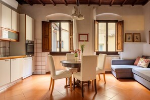 A modern kitchen with white cabinets, a dining table with chairs, and a sofa in a living area with large windows. - Casa Brunelleschi by Maison Florence (Florence)