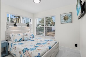Ein Schlafzimmer mit einem Bett, einem Nachttisch, einer Wandregal und einem Fenster mit Jalousien.
