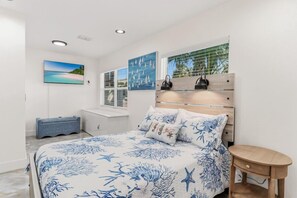 Quarto com cama, mesa de cabeceira, um banco e obras de arte nas paredes.