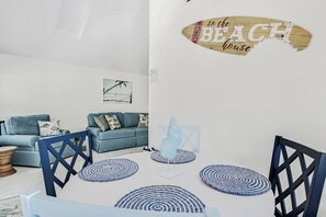 Ein modernes Wohnzimmer mit einem blauen Sofa, einem Couchtisch und einem Wandschild mit der Aufschrift 'WELCOME to the BEACH house'.