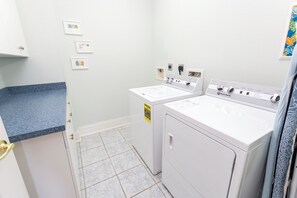 A laundry room with two front-loading washing machines, a countertop, and a door. - OCEANFRONT-Ocean Views, ELEV, Priv Pool, Hot Tub-S16, Voulez-Vous (Corolla)