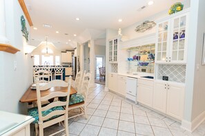 A kitchen with white cabinets, a dining area with a wooden table and chairs, and a tiled floor. - OCEANFRONT-Ocean Views, ELEV, Priv Pool, Hot Tub-S16, Voulez-Vous (Corolla)