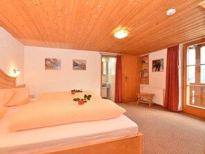 Ein Schlafzimmer mit Holzboden, einem Bett mit weißer Matratze, einem Nachttisch aus Holz und einem Fenster mit Vorhängen.