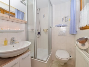 Ein Badezimmer mit einer Duschkabine, einem weißen Waschbecken, einer Toilette und einem Handtuchhalter mit Handtüchern.