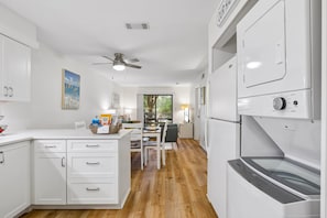A modern kitchen with white cabinetry, a ceiling fan, and a view into the dining area. - Fiddler's Cove Villa with Balcony, Tennis, Pickleball & Heated Community Pool (Hilton Head Island)