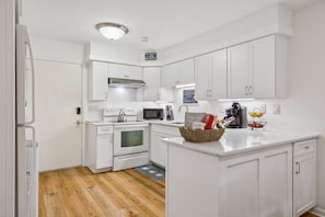 A modern kitchen with white cabinetry, a built-in oven, microwave, and a kettle on the stove. There is a coffee maker and a fruit basket on the counter. - Fiddler's Cove Villa with Balcony, Tennis, Pickleball & Heated Community Pool (Hilton Head Island)