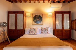 Habitació d'hotel amb un llit gran, dues taules laterals, un ventilador de peu i un quadre a la paret.