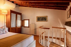 A bedroom with a wooden ceiling, a bed with a floral pillow, a radiator, and a painting on the wall. - Casa Masaccio by Maison Florence (Florence)