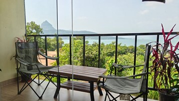 Varanda com mesa e duas cadeiras, com vista para uma paisagem exuberante e um corpo d'água.