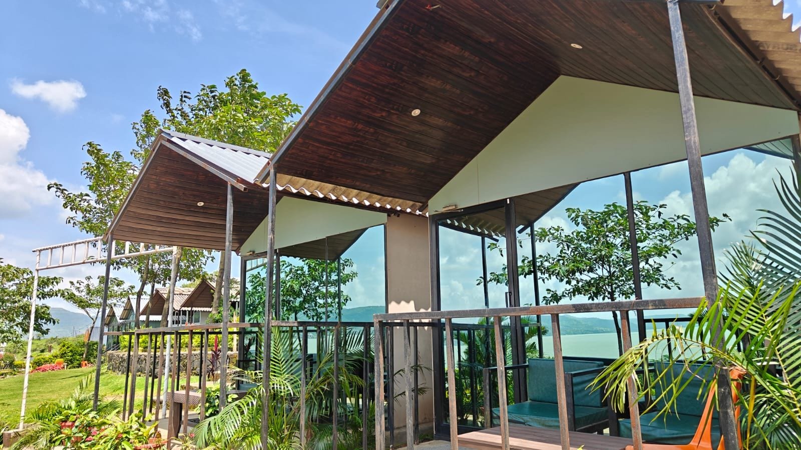 A modern outdoor structure with a glass enclosure, surrounded by lush greenery and a view of a body of water.