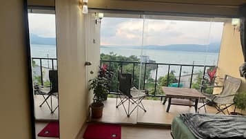 A room with a bed, a mirror, a balcony with a view of the sea, and a potted plant.