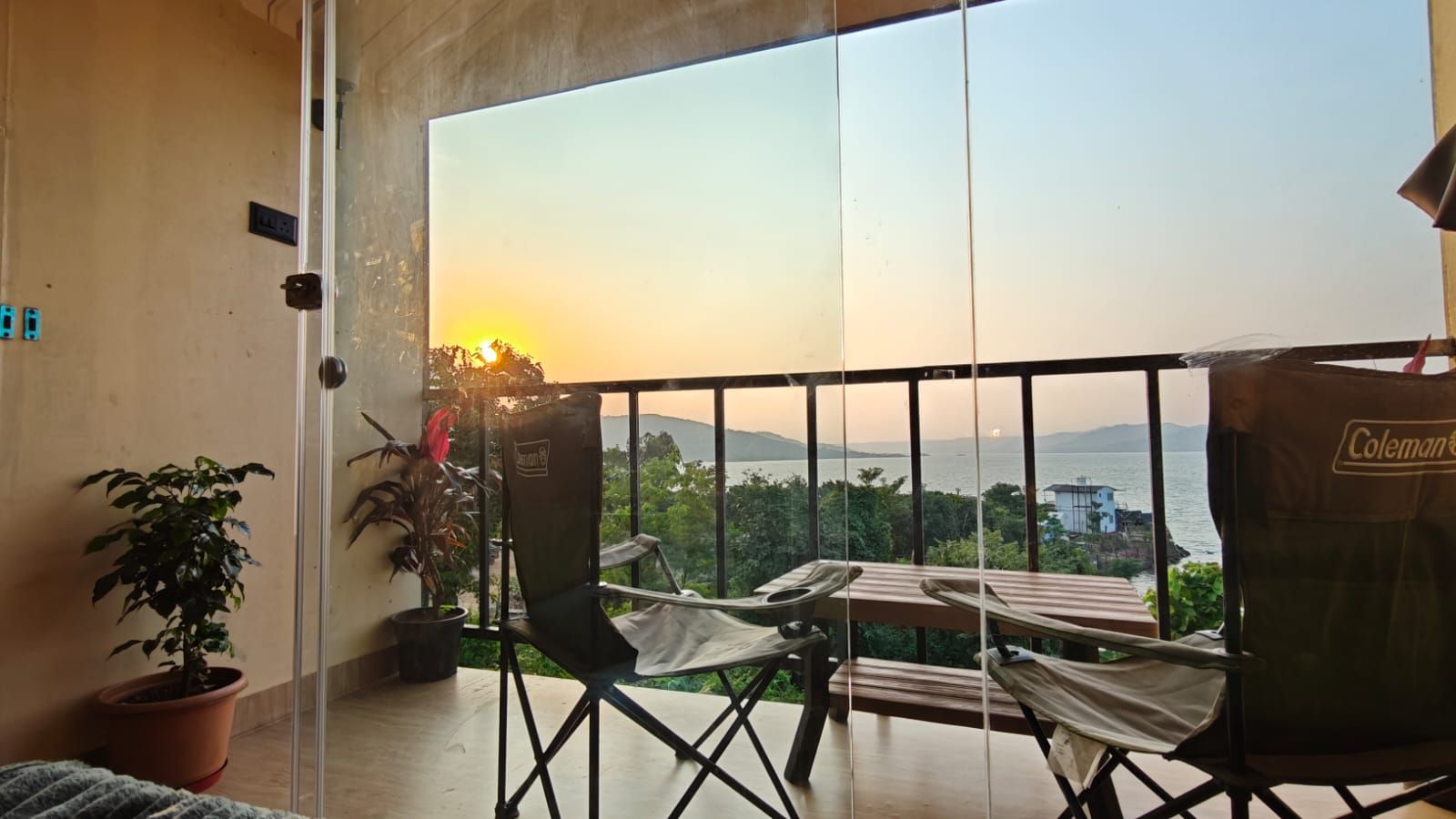 A balcony with a view of the sea, a table, two chairs, and a potted plant.