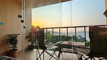 A balcony with a view of the sea, a table, two chairs, and a potted plant.