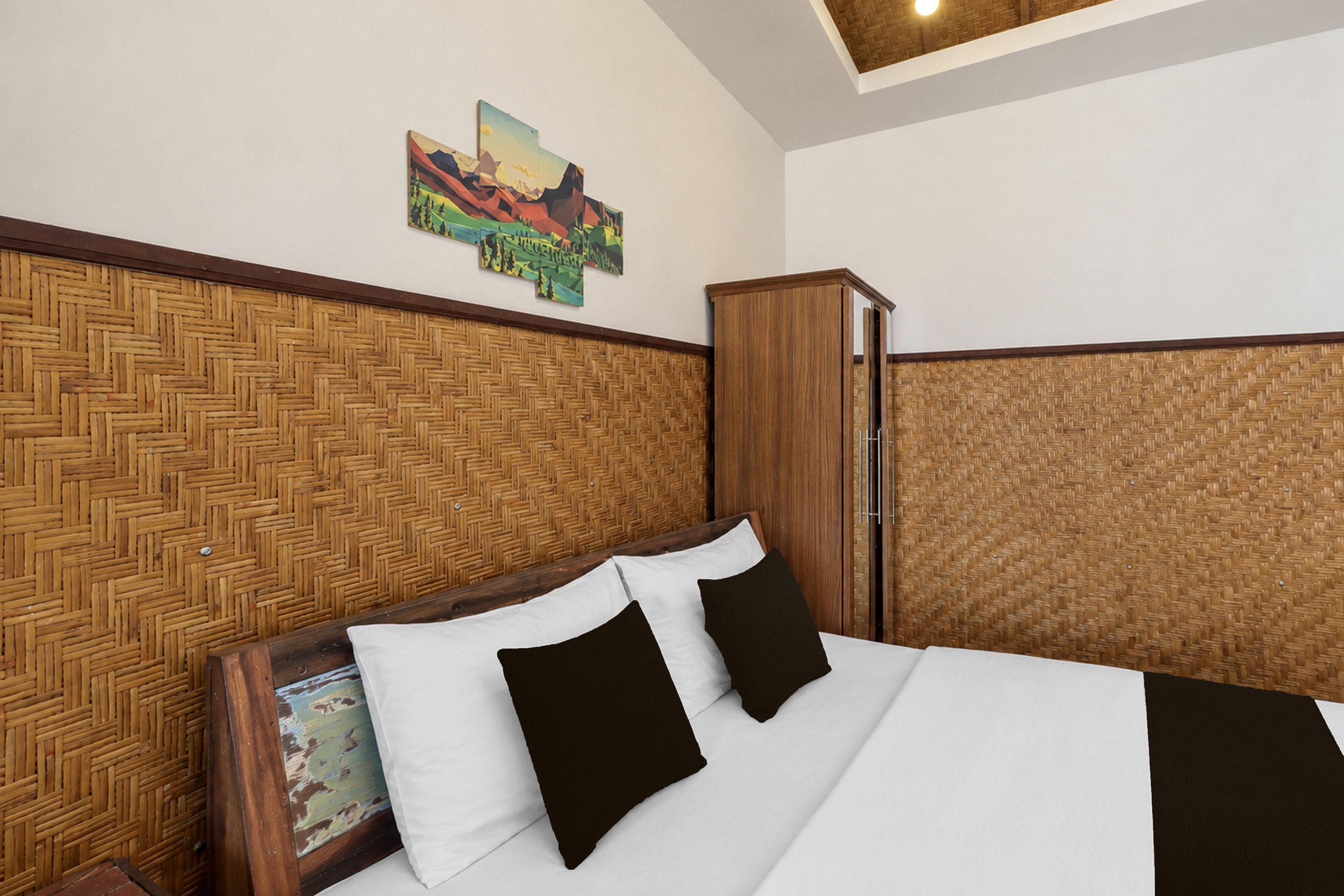 Une chambre d’hôtel avec une tête de lit à motifs en chevrons, un lit avec du linge de maison blanc et des oreillers noirs, et une armoire en bois.