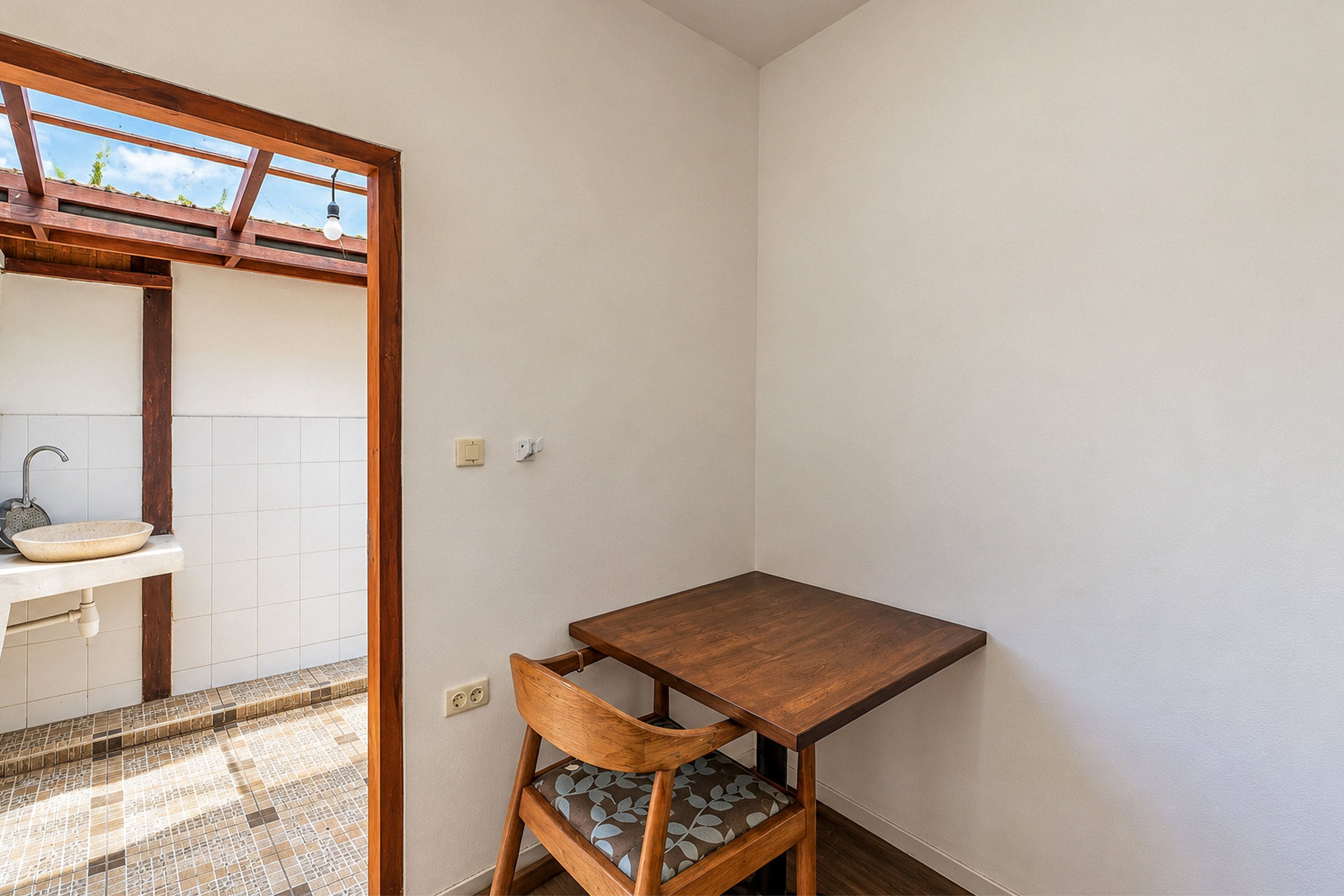 Une petite pièce avec une table en bois, une chaise, un évier et un sol carrelé.