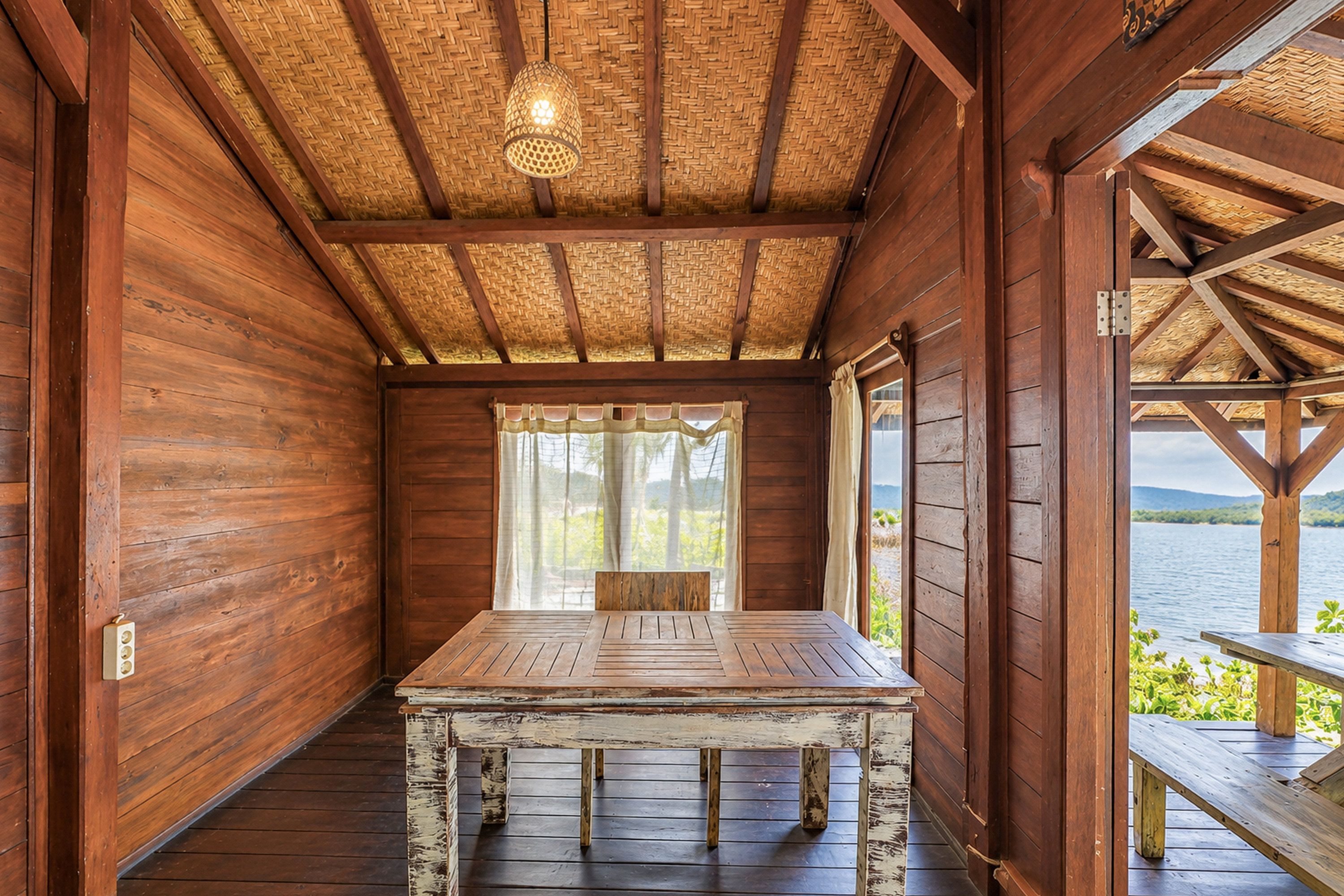Une cabane en bois avec une table et un banc, un toit de chaume et une vue sur un lac.