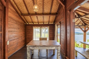A wooden cabin with a table and bench, a thatched roof, and a view of a lake. - Collection O Surya Abadi Guest House  (Tibubeneng)
