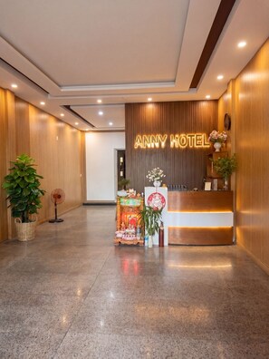 Een hotel receptie met een houten balie, een wandbord en een klein altaar met aanbiedingen.