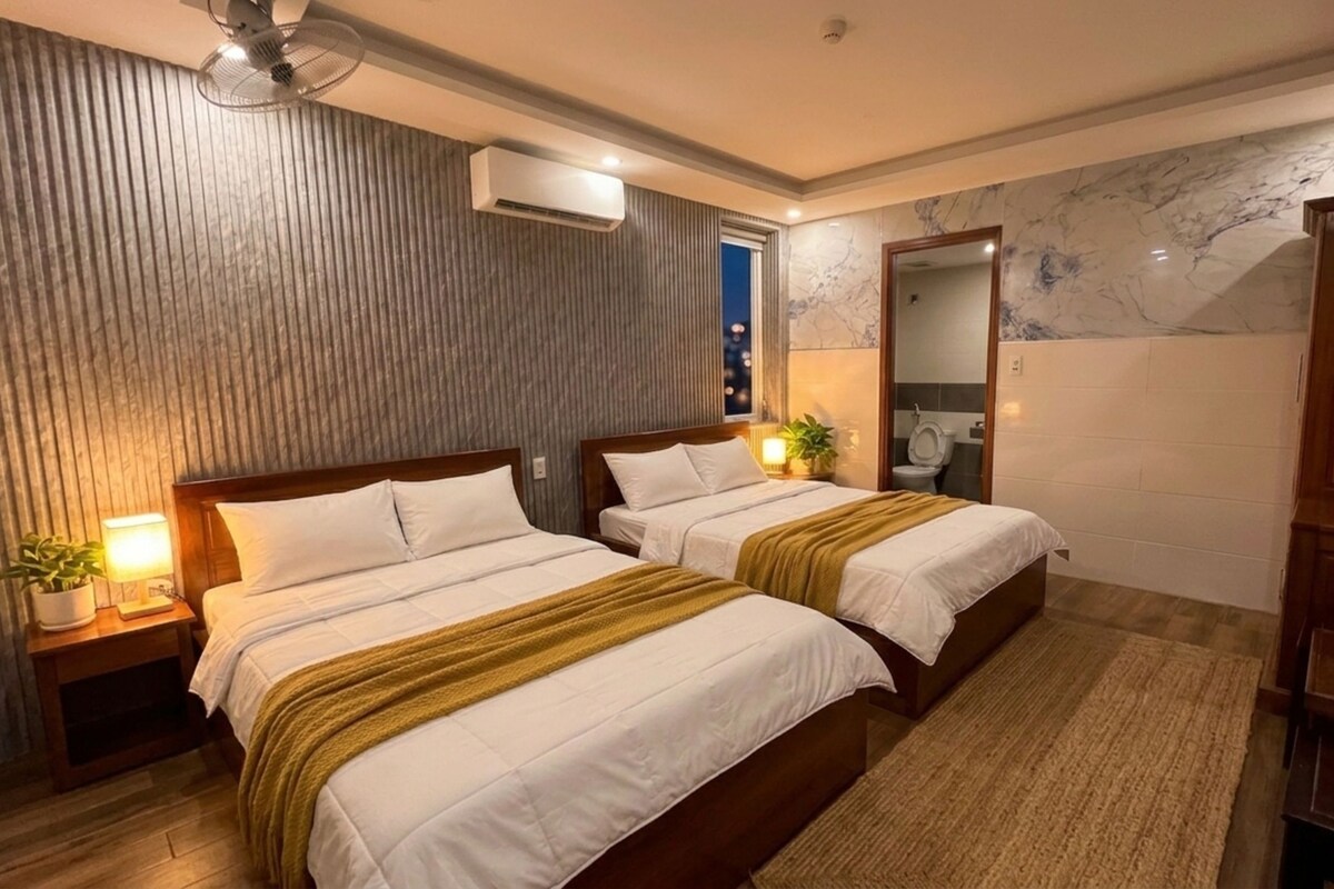 Een hotelkamer met twee bedden, een houten hoofdbord, een spiegel, een houten garderobe en een plant in een pot.
