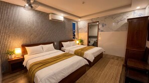 Een hotelkamer met twee bedden, een houten hoofdbord, een spiegel, een houten garderobe en een plant in een pot.