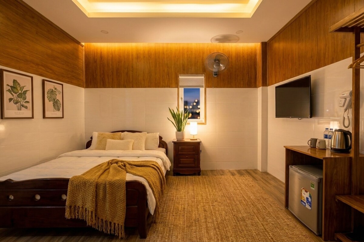 Een hotelkamer met een bed, nachtkastje, lamp, televisie en een kleine keukenhoek.
