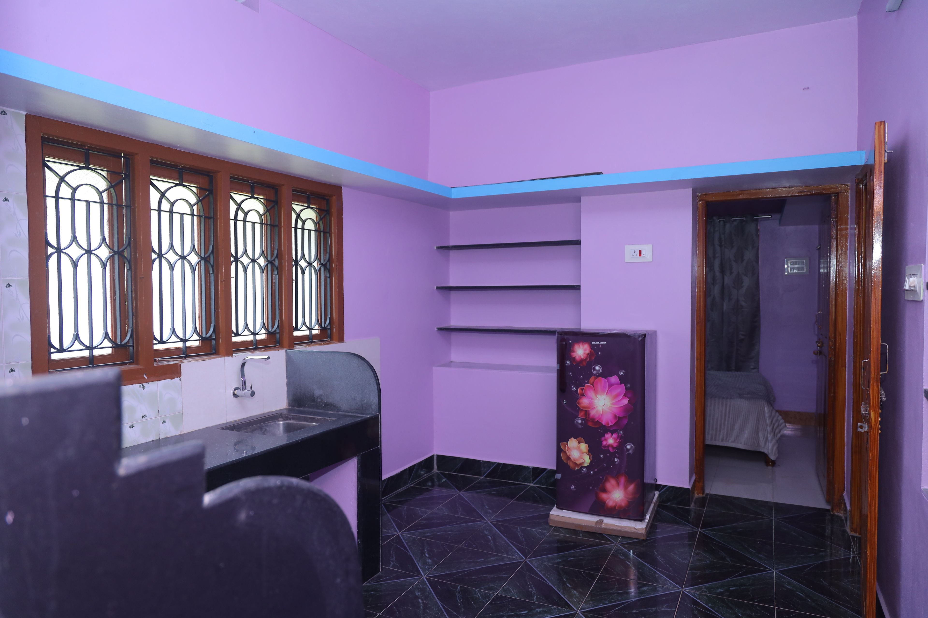 A room with a black tiled floor, a window with metal bars, a sink, a cabinet with a floral design, and a door leading to another room.