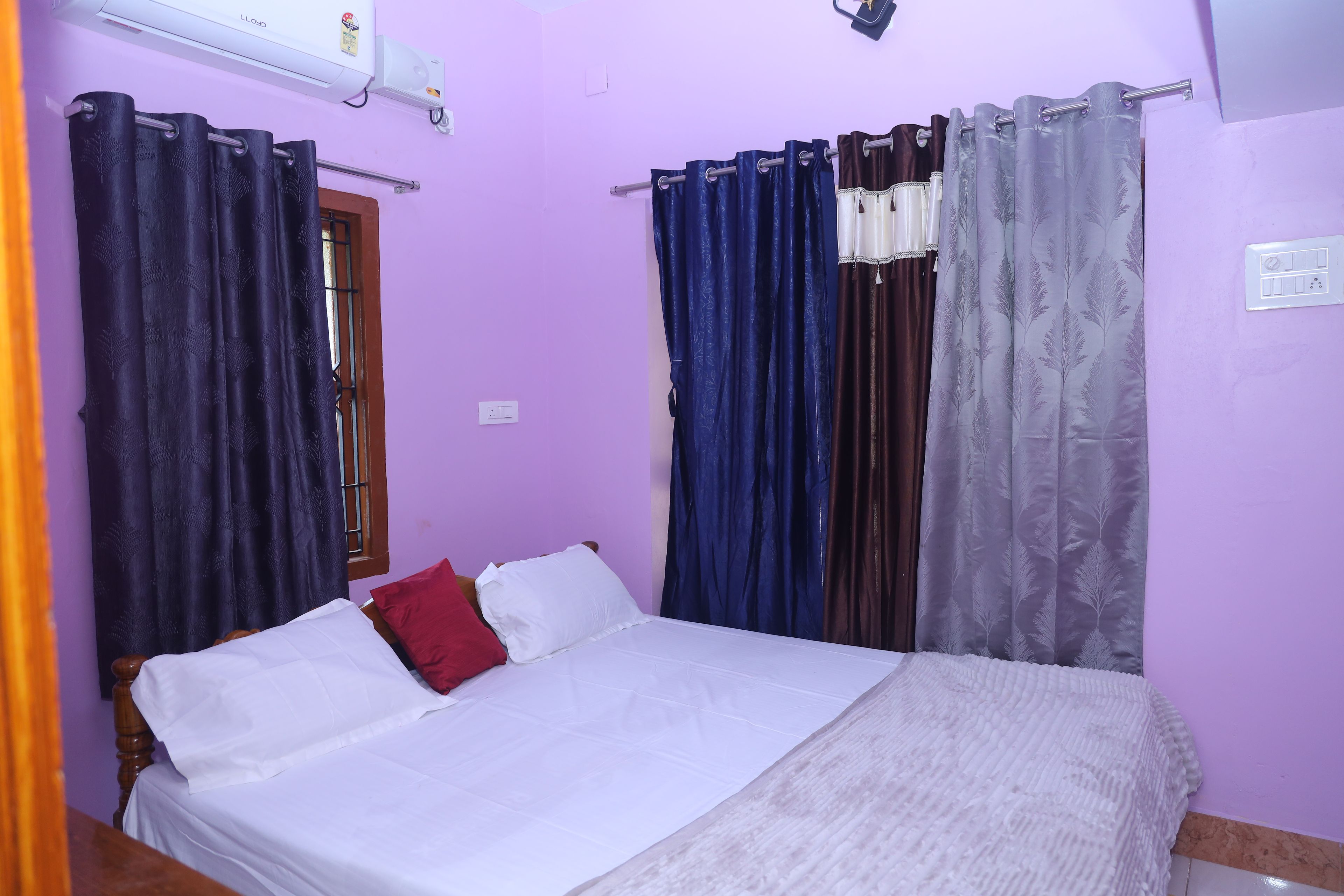 A room with a bed, curtains, an air conditioning unit, and a window with a metal grill.