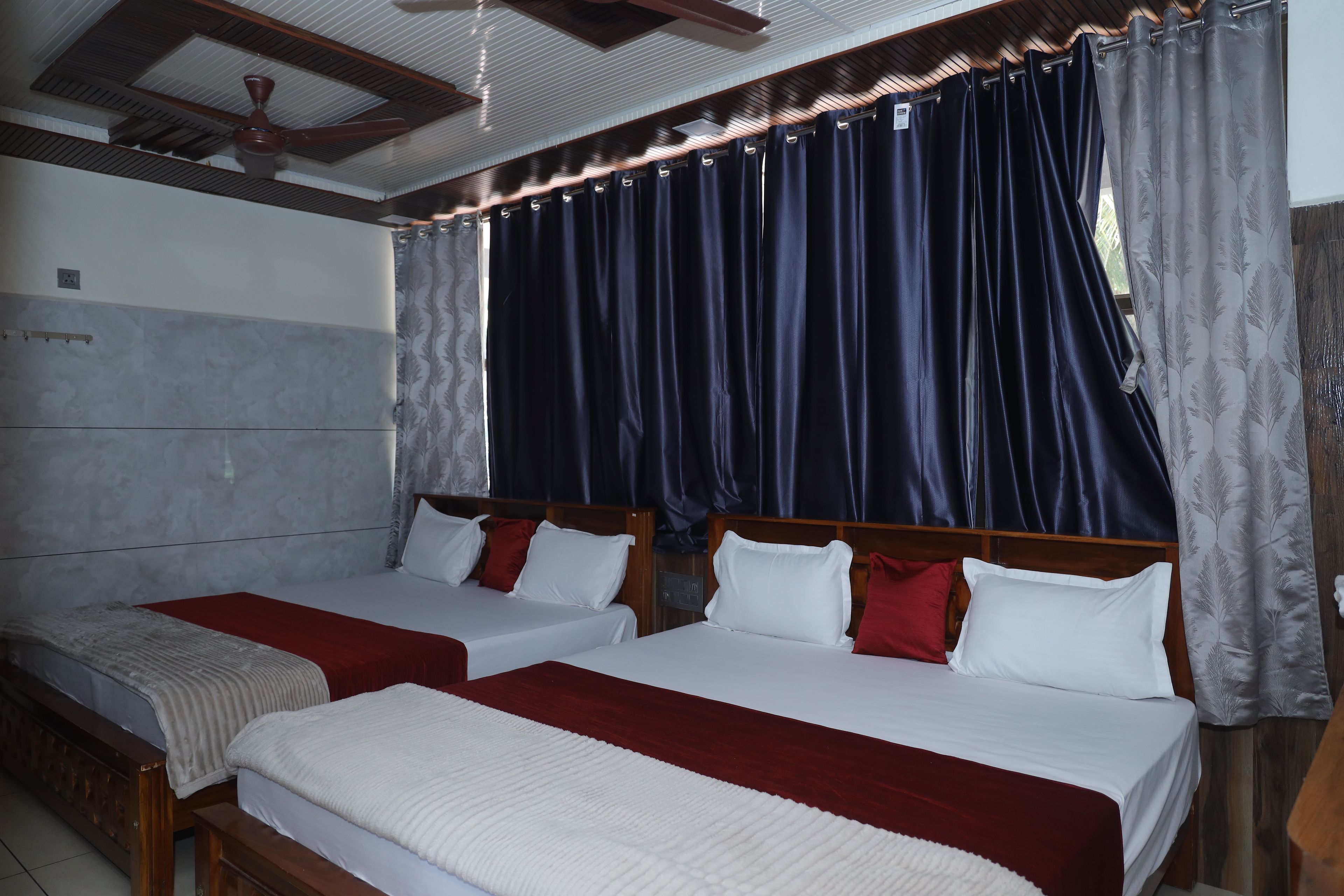 Habitación de hotel con dos camas, ventilador de techo y ventana con cortinas oscuras.