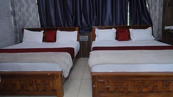 A hotel room with two wooden beds, white bedding, red and white pillows, and dark curtains.