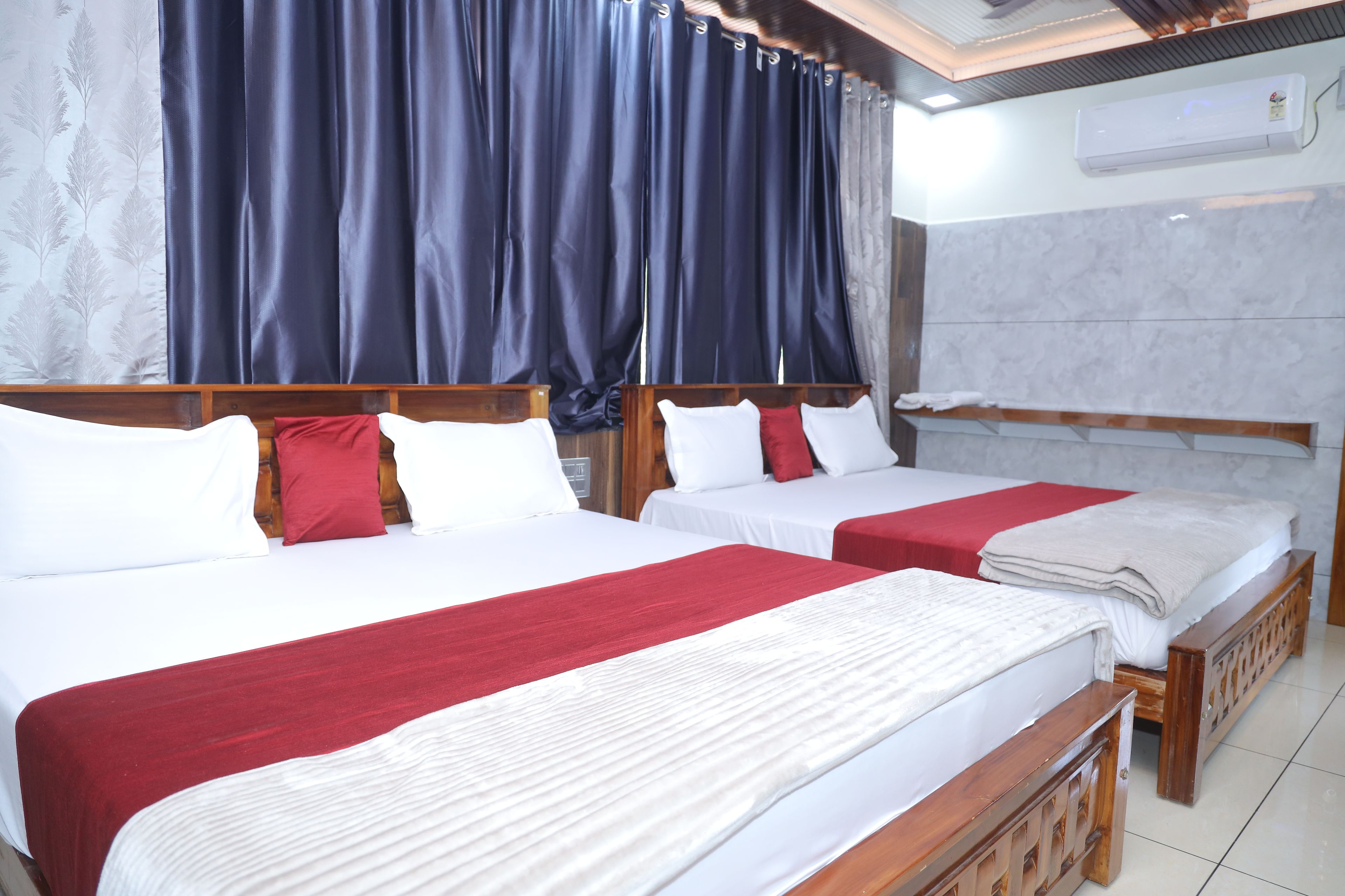 Habitación de hotel con dos camas, cada una con ropa de cama blanca y detalles rojos, un cabecero de madera y un ventanal con cortinas oscuras.