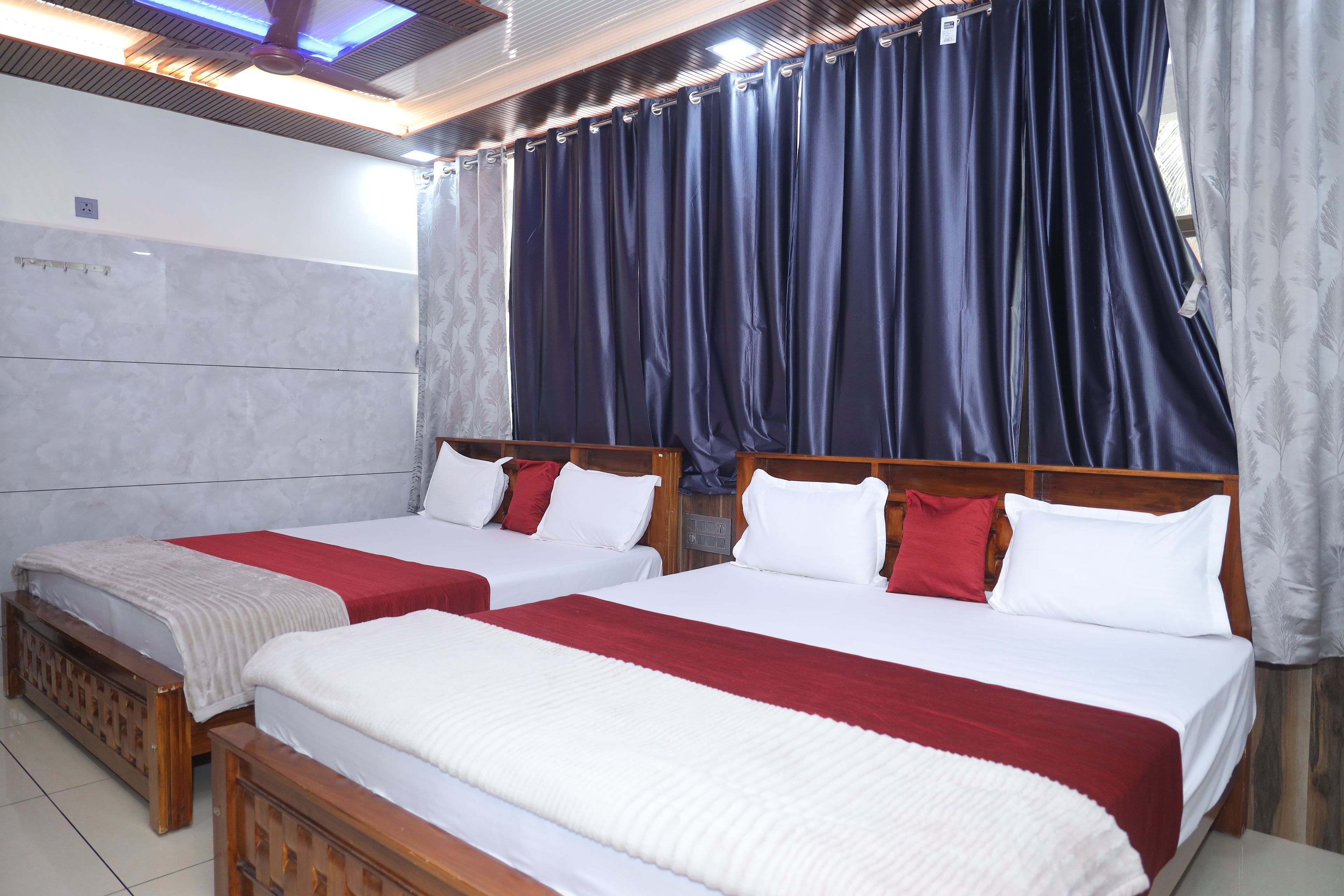 A hotel room with two beds, a wooden headboard, a red and white bedspread, and a large window with curtains.