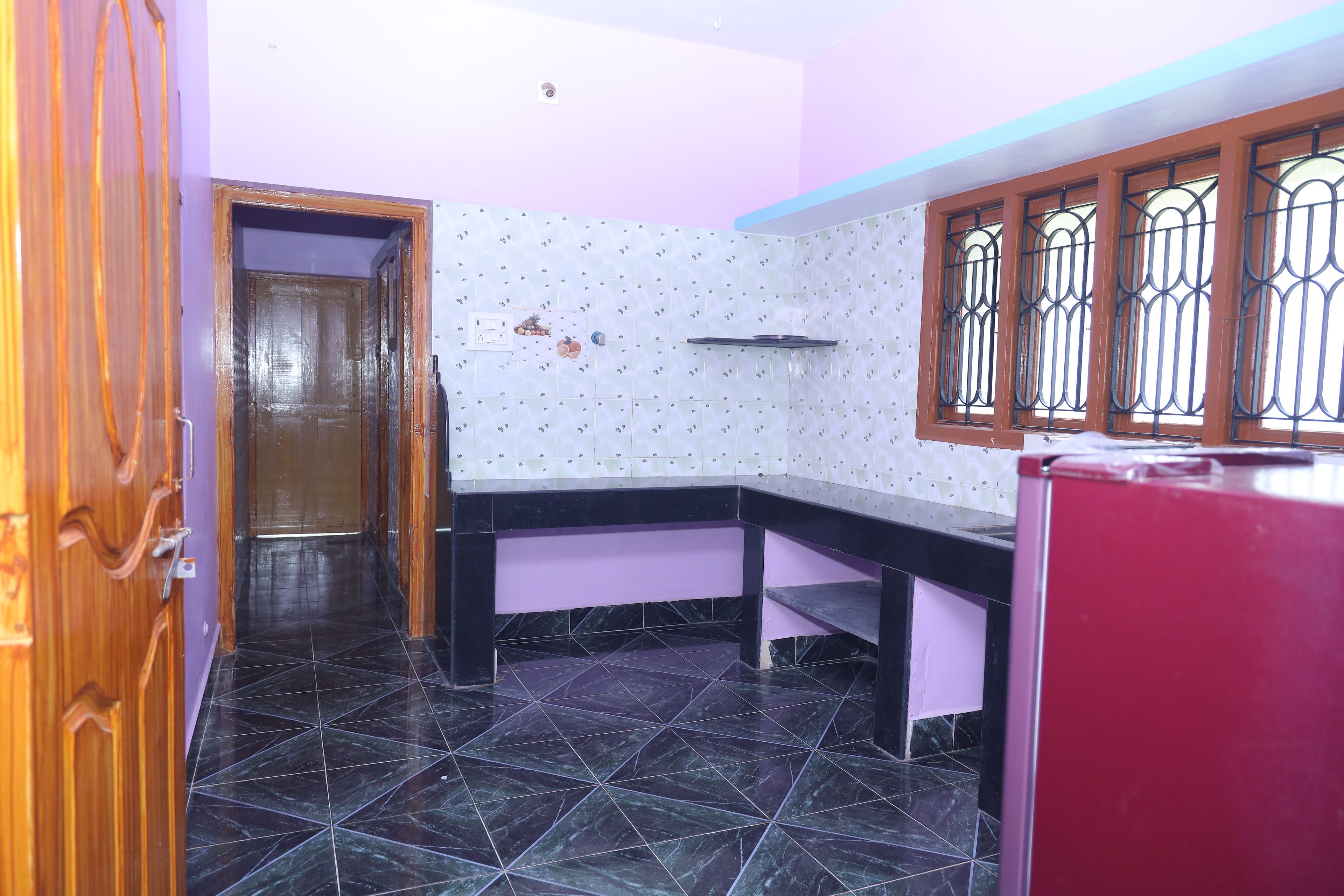 Una cocina con piso de baldosas negras, una puerta de madera, una pared morada y una ventana con barrotes de metal.