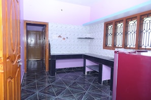 Una cocina con piso de baldosas negras, una puerta de madera, una pared morada y una ventana con barrotes de metal.