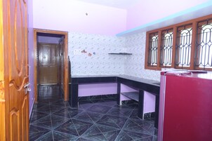 Una cocina con piso de baldosas negras, una puerta de madera, una pared morada y una ventana con barrotes de metal.