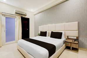 A hotel room with a large bed, a nightstand, an air conditioning unit, and a door with curtains. - Townhouse Hotel Sec- 54 Golf Course Road (Gurugram)