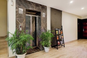 An elevator with a digital display, a potted plant, and a book rack in a lobby area. - Townhouse Hotel Sec- 54 Golf Course Road (Gurugram)