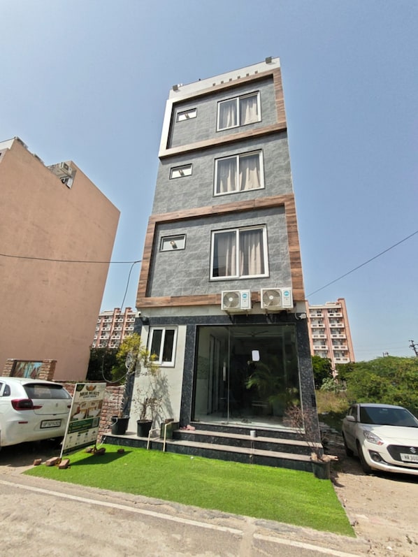 A multi-story residential building with a modern design, featuring a flat roof, large windows, and a visible entrance with steps leading up to it. - SRG Hotel and Restruant (Mathura)