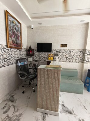 A reception area with a marble floor, a reception desk, a television mounted on the wall, and a patterned wall design. - SRG Hotel and Restruant (Mathura)