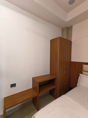 A bedroom with a bed, a wooden wardrobe, and a small wooden shelf unit. - SRG Hotel and Restruant (Mathura)