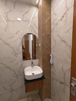 A bathroom with a marble wall, a sink with a mirror, and a wooden vanity. - SRG Hotel and Restruant (Mathura)
