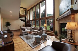 Un salón amplio con un ventanal grande, una chimenea, una escalera y una zona de estar acogedora.