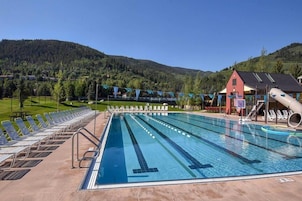 Una piscina con múltiples carriles, tumbonas y un tobogán.