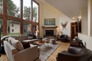 A spacious living room with a fireplace, large windows, and a view of a house. - C8 Cornerstone Condos 3 Bedroom Condo (Avon)
