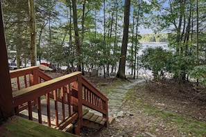 A wooden deck with a stone pathway leading to a lake surrounded by trees. - Lakefront w/ Private Shoreline | Kayaks + Paddle Boards + Firepit | Covewood (Lakeville)