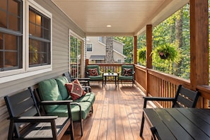 A covered porch with wooden flooring, green cushioned seating, and a stone fireplace. - Lakefront w/ Private Shoreline | Kayaks + Paddle Boards + Firepit | Covewood (Lakeville)