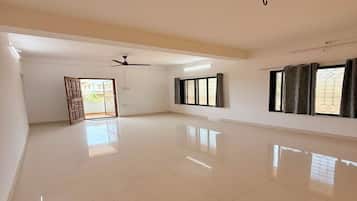 A spacious room with a high ceiling, a ceiling fan, and a large window with curtains.