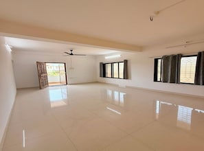 A spacious room with a high ceiling, a ceiling fan, and a large window with curtains. - Stella Casa (Ratnagiri)
